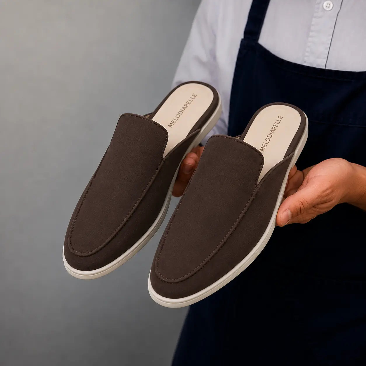 Man holding a pair of Melodiapelle Mole Mule shoes in dark brown suede, close-up