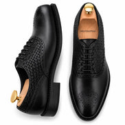 Man holding a pair of Melodiapelle Monaldo Woven Brogue Oxford shoes in black leather, close-up