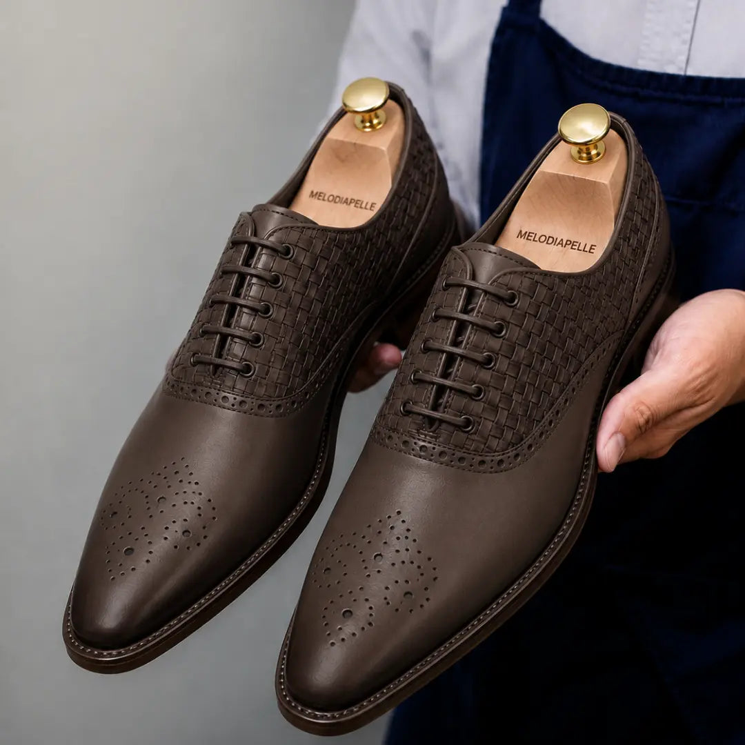 Man holding a pair of Melodiapelle Monaldo Woven Brogue Oxford shoes in brown leather, close-up