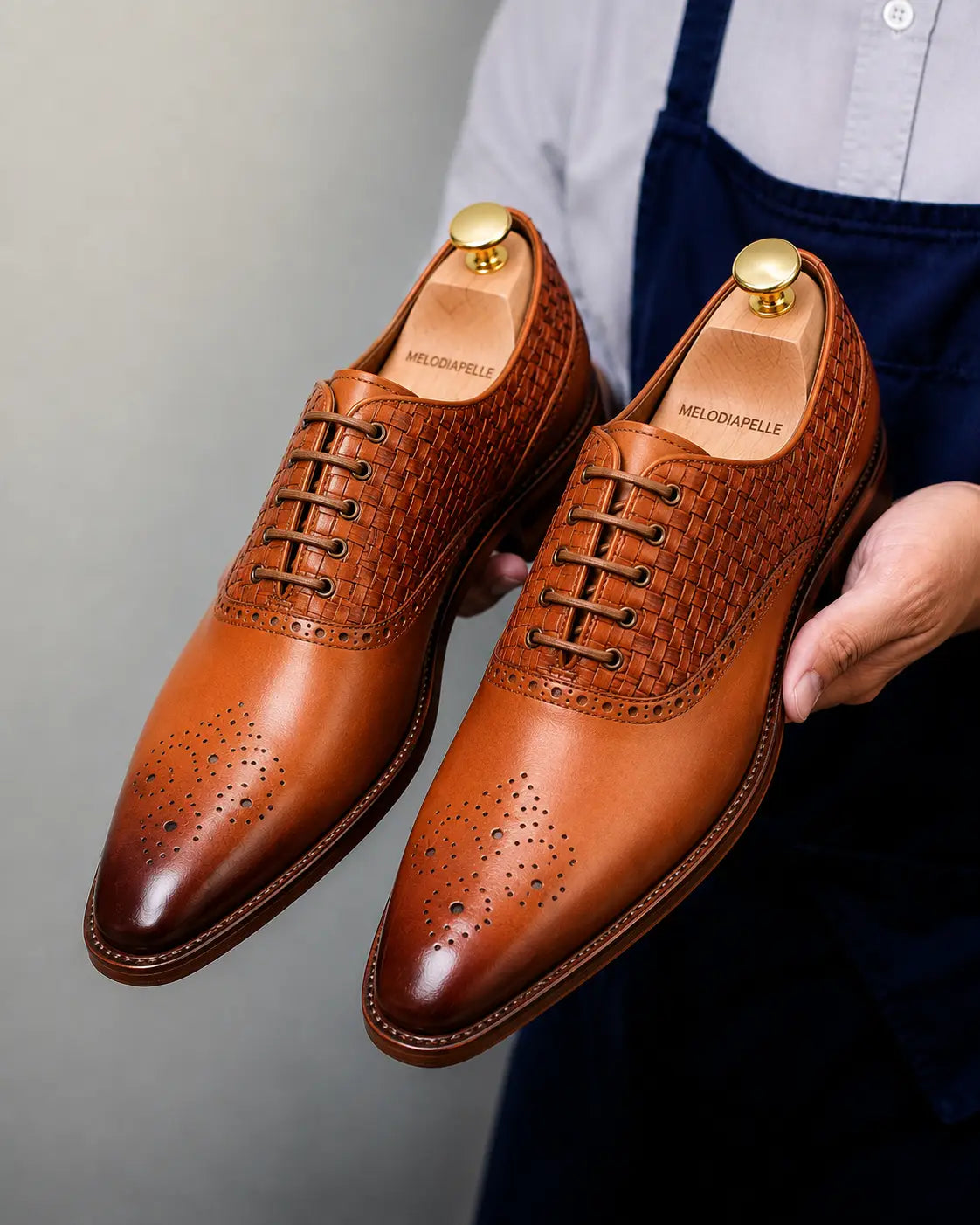 Man holding a pair of Melodiapelle Monaldo Woven Brogue Oxford shoes in honey cognac leather, close-up
