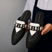Man holding a pair of Melodiapelle Monatella Mule shoes in black and white woven leather, close-up