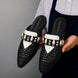 Man holding a pair of Melodiapelle Monatella Mule shoes in black and white woven leather, close-up