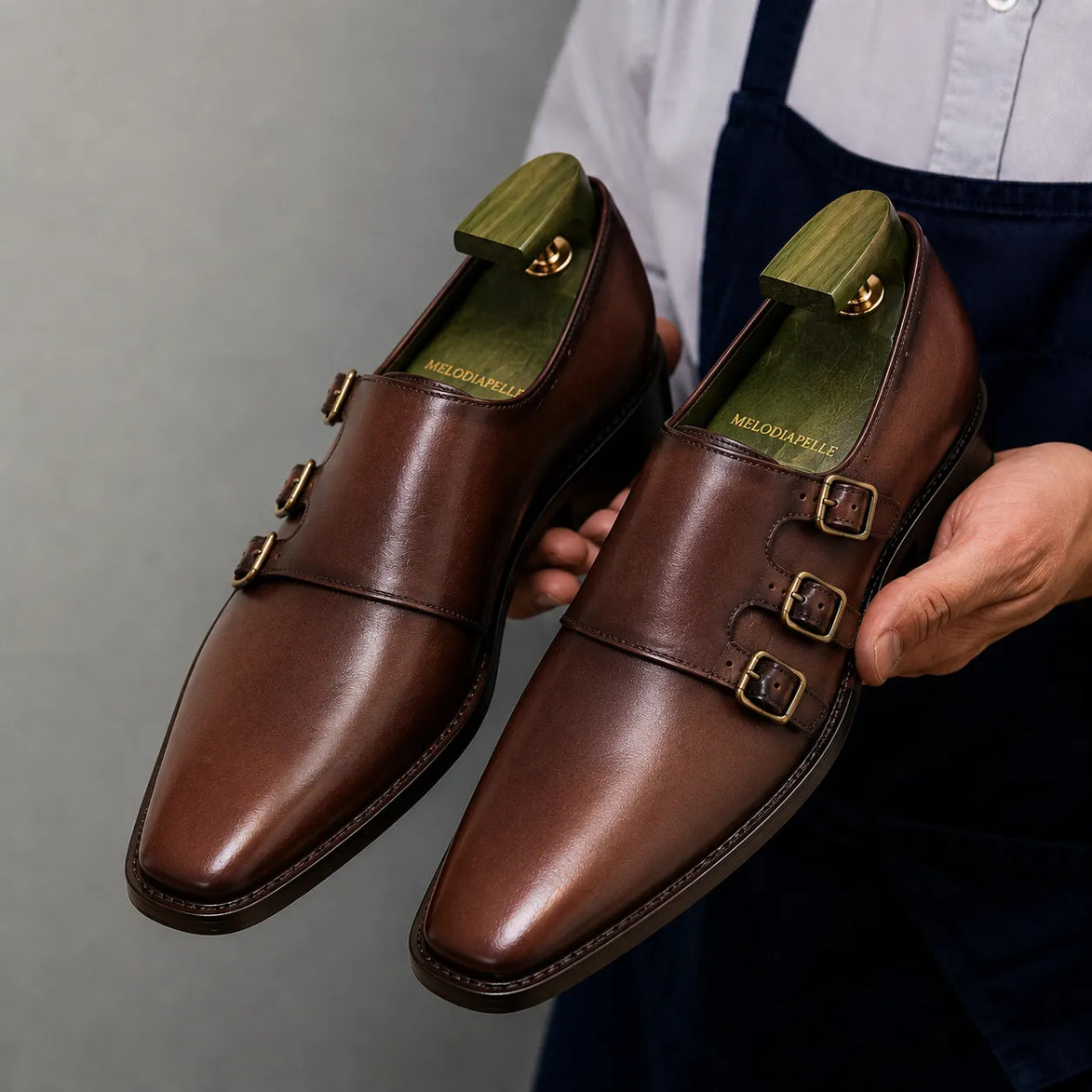 Man holding a pair of Melodiapelle Montecito Double Monk Strap shoes in dark chocolate leather, close-up