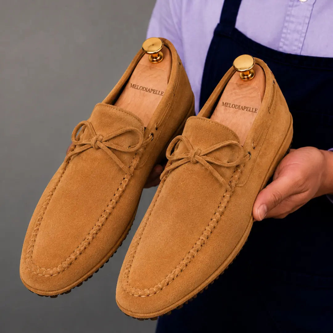 Man holding a pair of Melodiapelle Montgomery Loafers in camel tan suede, close-up