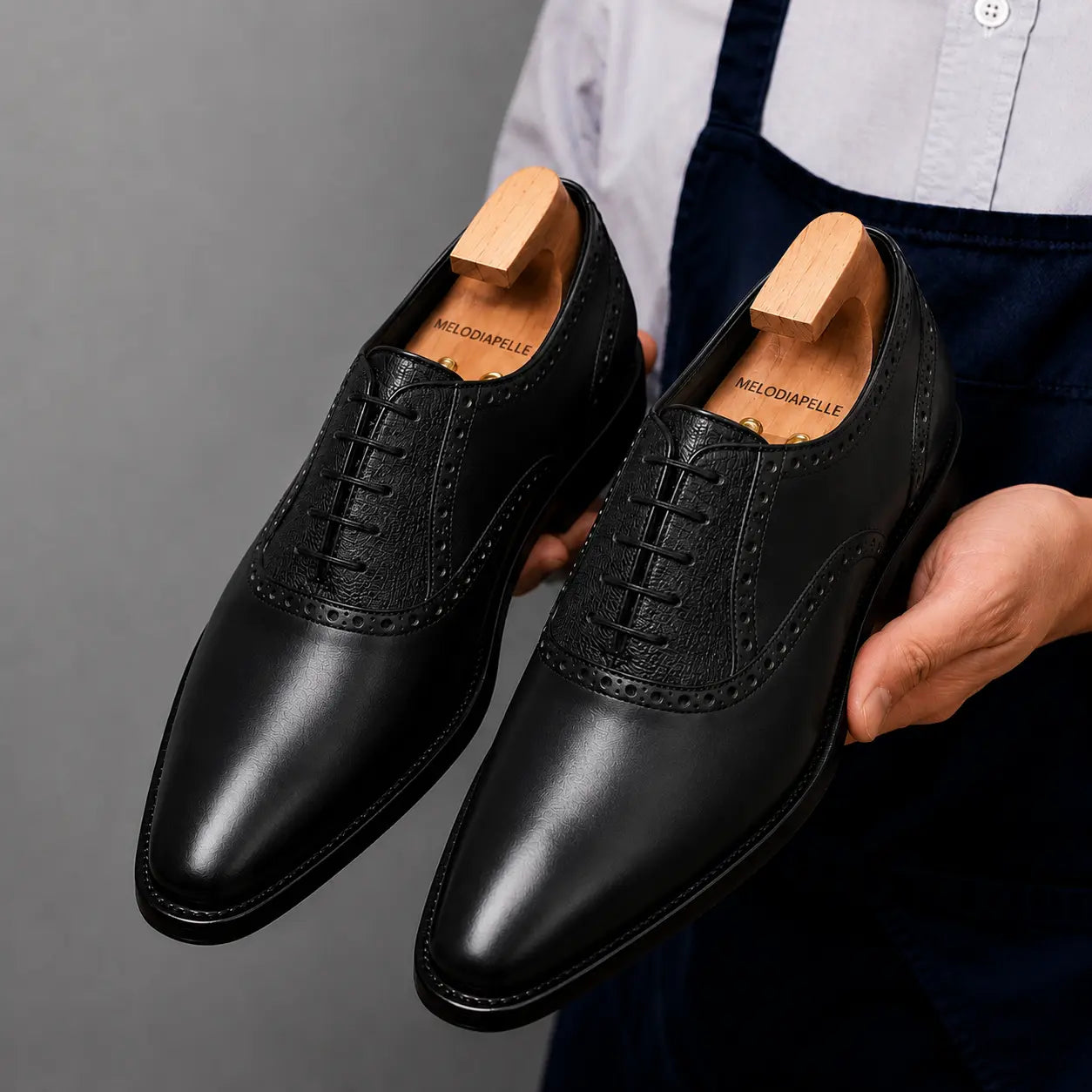 Man holding a pair of Melodiapelle Montserrat Two-Tone Saddle Oxford shoes in black leather, close-up