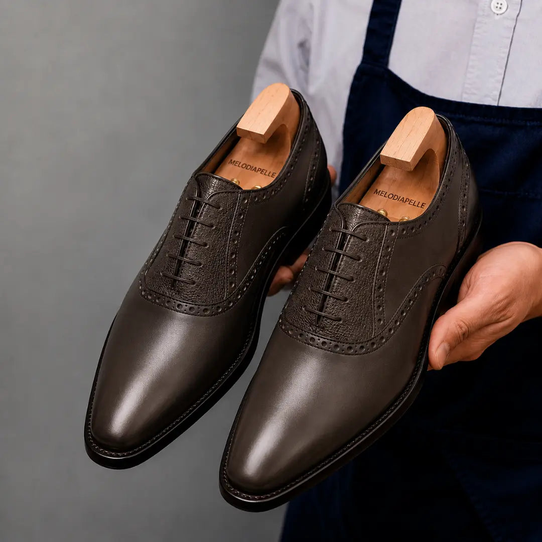 Man holding a pair of Melodiapelle Montserrat Two-Tone Saddle Oxford shoes in brown leather, close-up