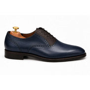 Side profile of the Montserrat Two-Tone Saddle Oxford in navy and dark brown leather on white background
