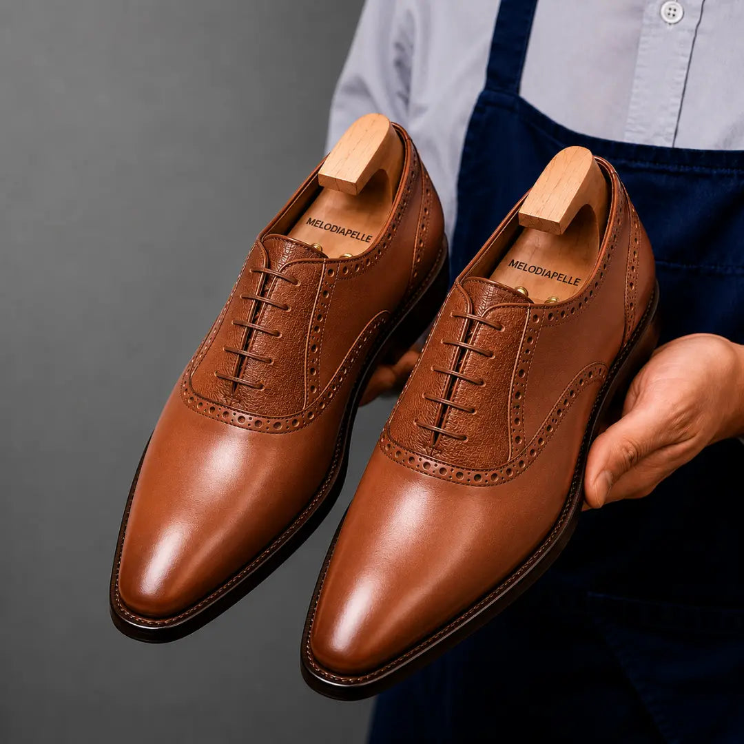Man holding a pair of Melodiapelle Montserrat Two-Tone Saddle Oxford shoes in tan leather, close-up