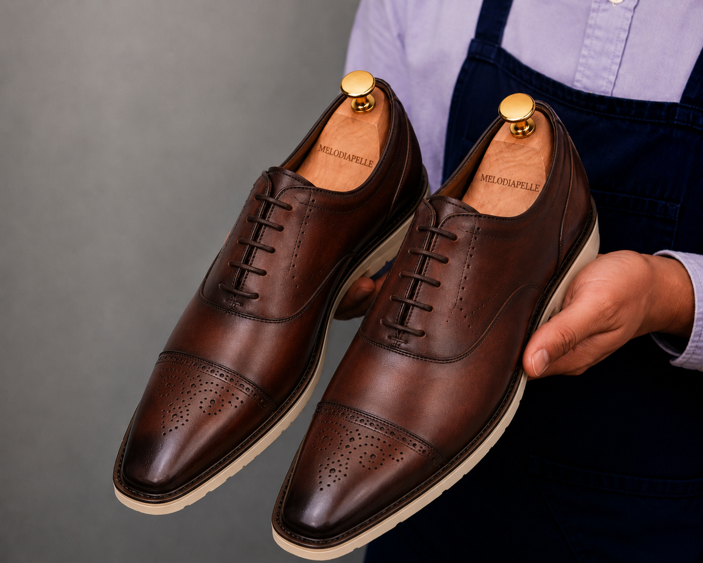 Man holding a pair of Melodiapelle Moorland Cap-Toe Derby shoes in dark chocolate leather, close-up