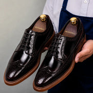 Man holding a pair of Melodiapelle Morano Wingtip Brogue Derby shoes in oxblood brown leather, close-up