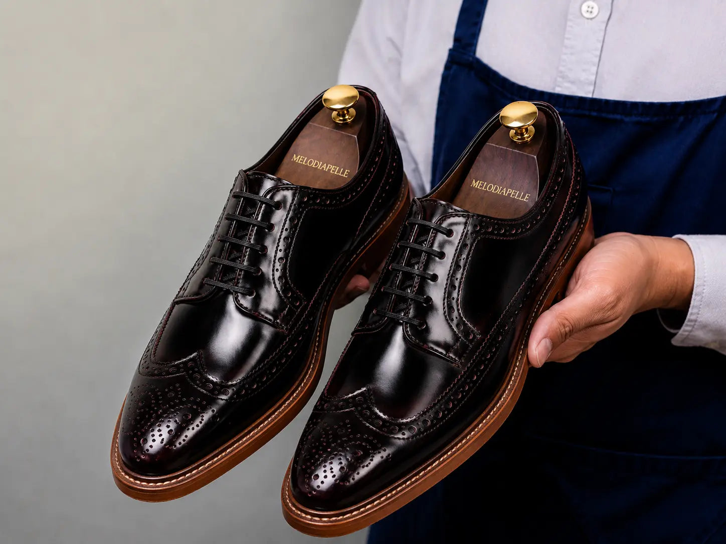 Man holding a pair of Melodiapelle Morano Wingtip Brogue Derby shoes in oxblood brown leather, close-up
