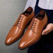 Man holding a pair of Melodiapelle Morano Wingtip Brogue Derby shoes in tan leather, close-up