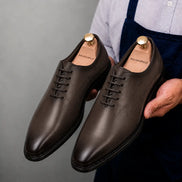 Man holding a pair of Melodiapelle Mordecai Script Wholecut Oxford shoes in brown leather, close-up