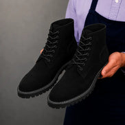 Man holding a pair of Melodiapelle Moreno Combat Boots in black suede, close-up