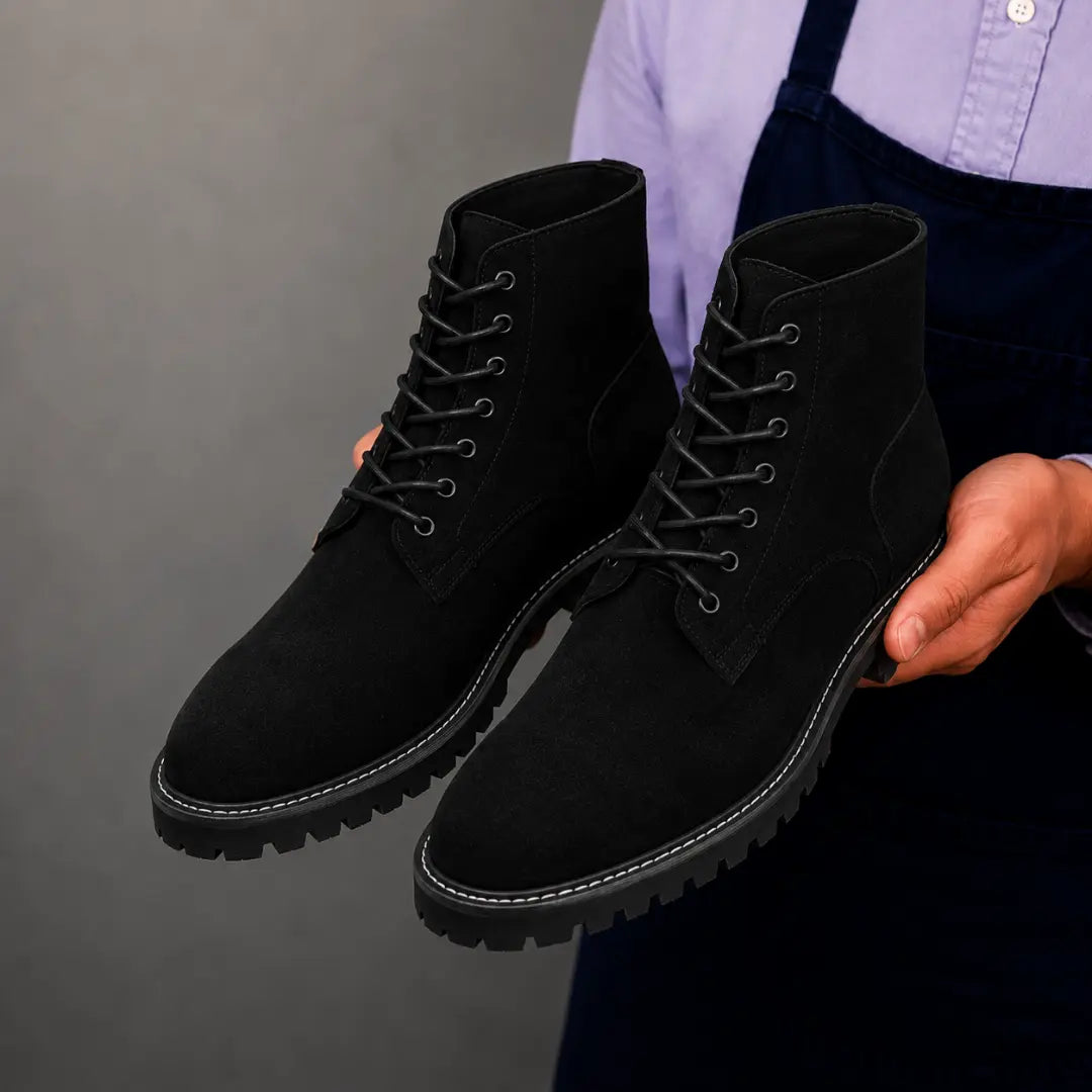 Man holding a pair of Melodiapelle Moreno Combat Boots in black suede, close-up