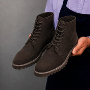 Man holding a pair of Melodiapelle Moreno Combat Boots in dark brown suede, close-up