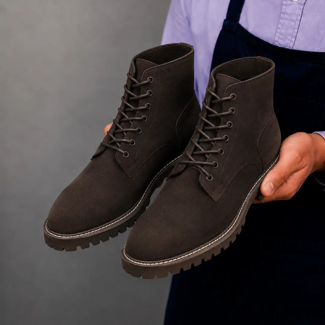 Man holding a pair of Melodiapelle Moreno Combat Boots in dark brown suede, close-up