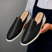 Man holding a pair of Melodiapelle Moreno Mule shoes in black croc-embossed leather, close-up