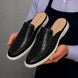 Man holding a pair of Melodiapelle Moreno Mule shoes in black croc-embossed leather, close-up