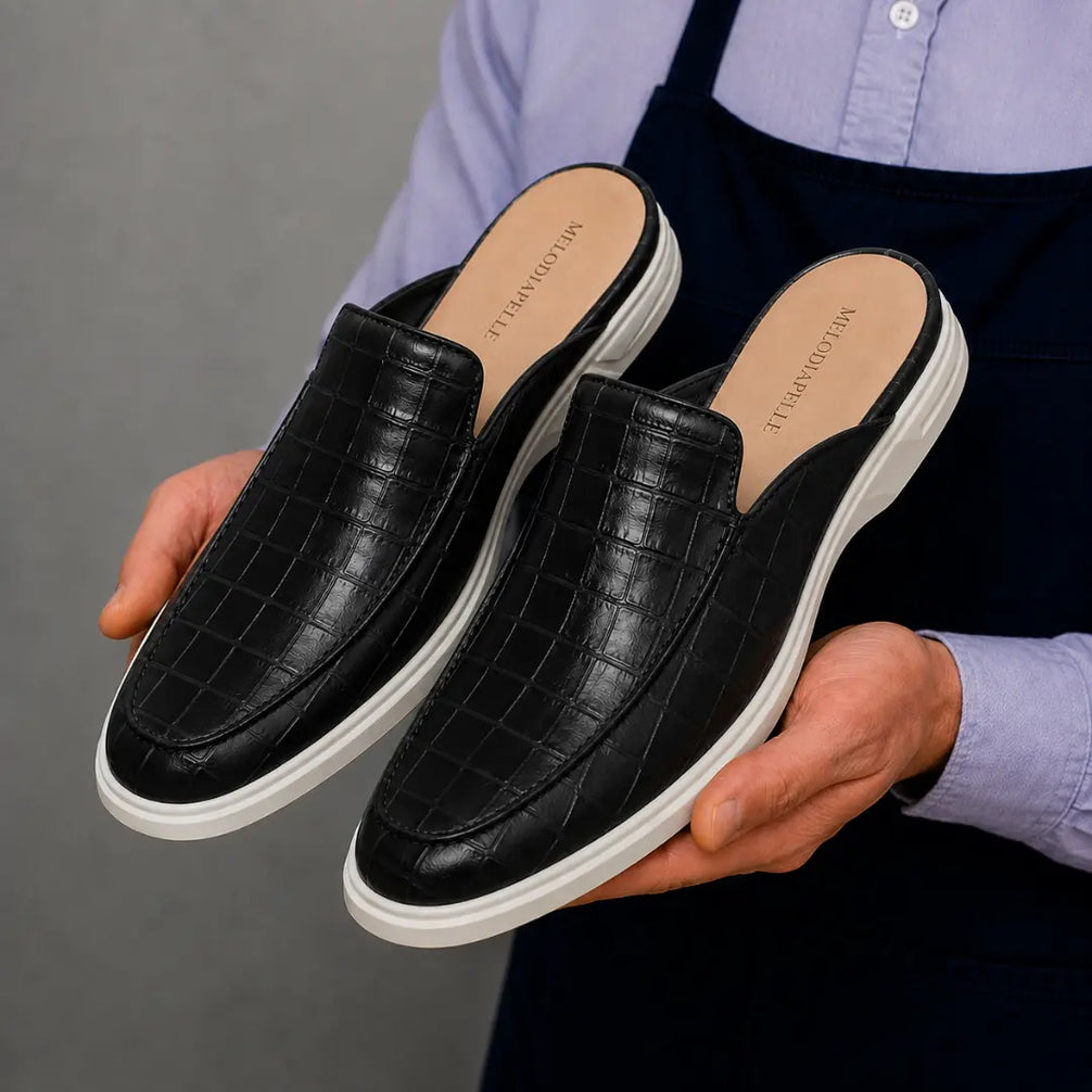 Man holding a pair of Melodiapelle Moreno Mule shoes in black croc-embossed leather, close-up