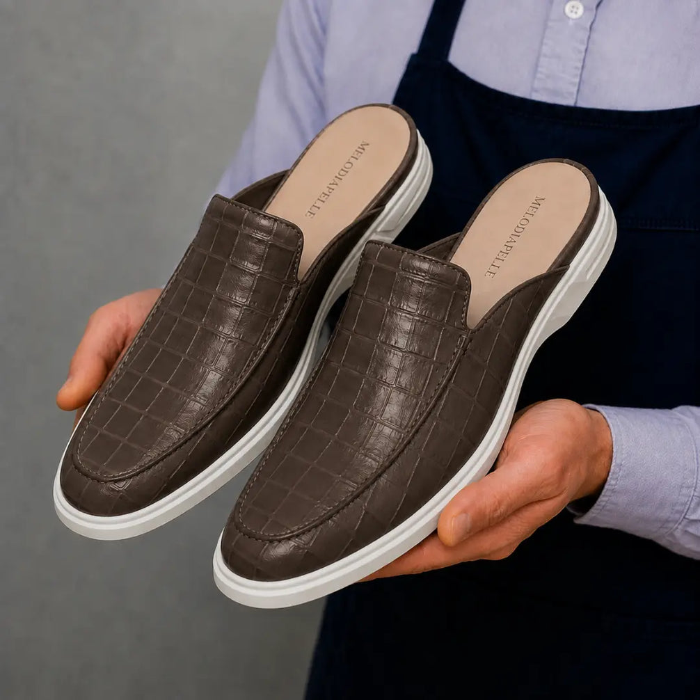 Man holding a pair of Melodiapelle Moreno Mule shoes in dark brown croc-embossed leather, close-up