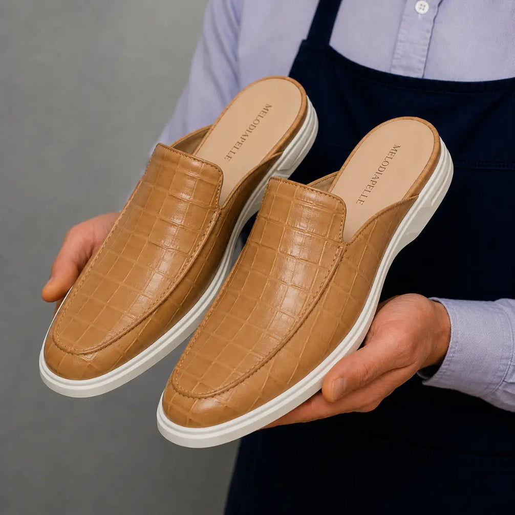 Man holding a pair of Melodiapelle Moreno Mule shoes in sand beige croc-embossed leather, close-up