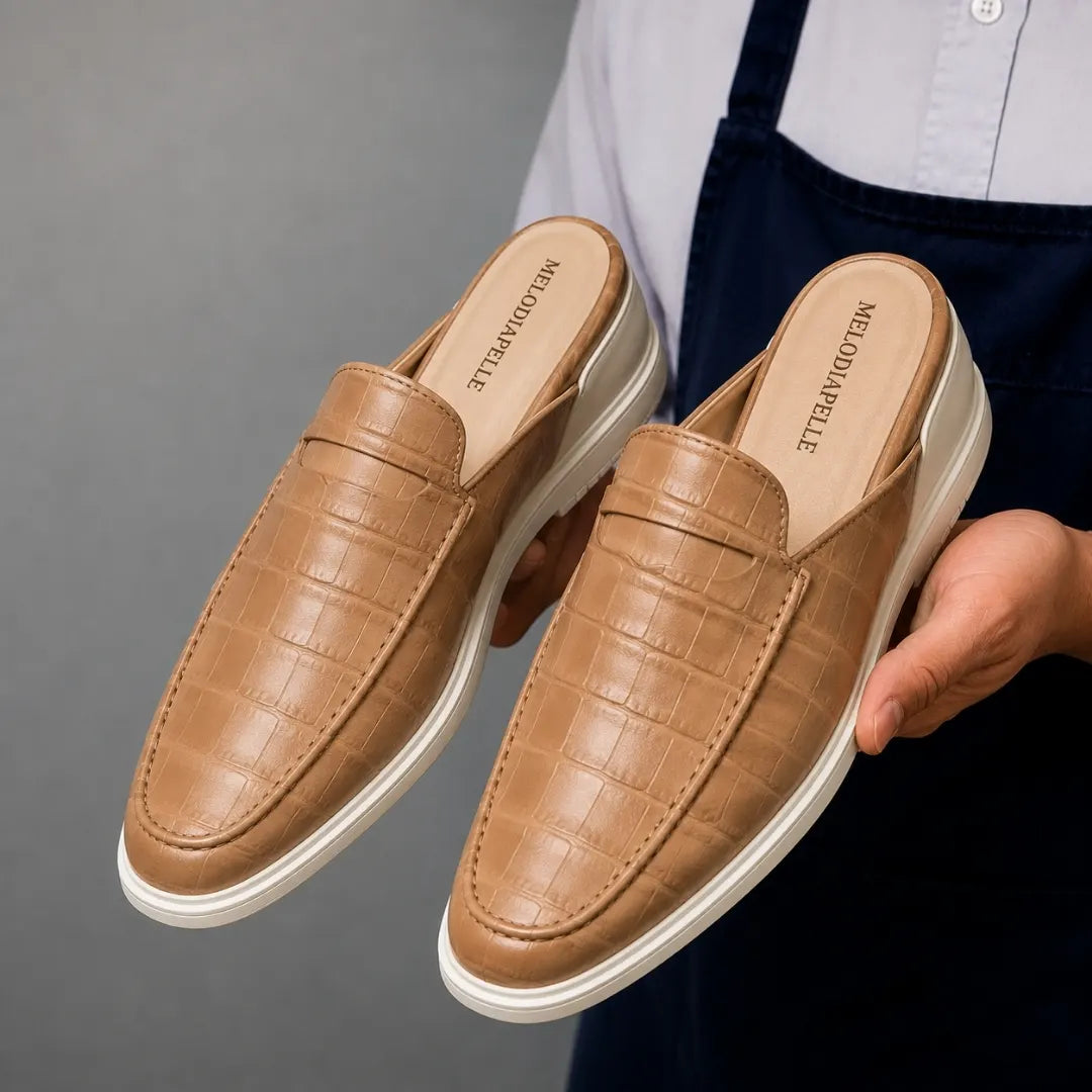 Man holding a pair of Melodiapelle Moreno Mule shoes in sand beige croc-embossed leather, close-up