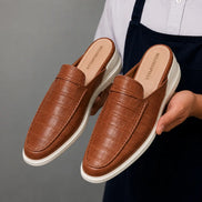 Man holding a pair of Melodiapelle Moreno Mule shoes in tan croc-embossed leather, close-up
