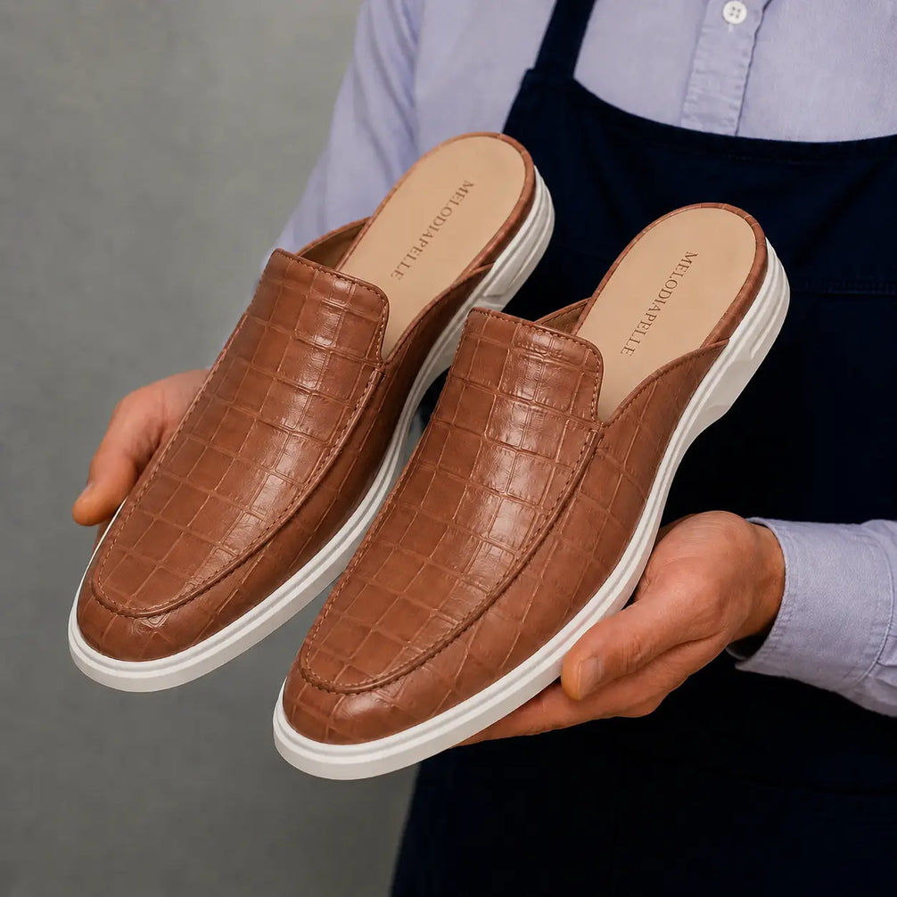 Man holding a pair of Melodiapelle Moreno Mule shoes in tan croc-embossed leather, close-up