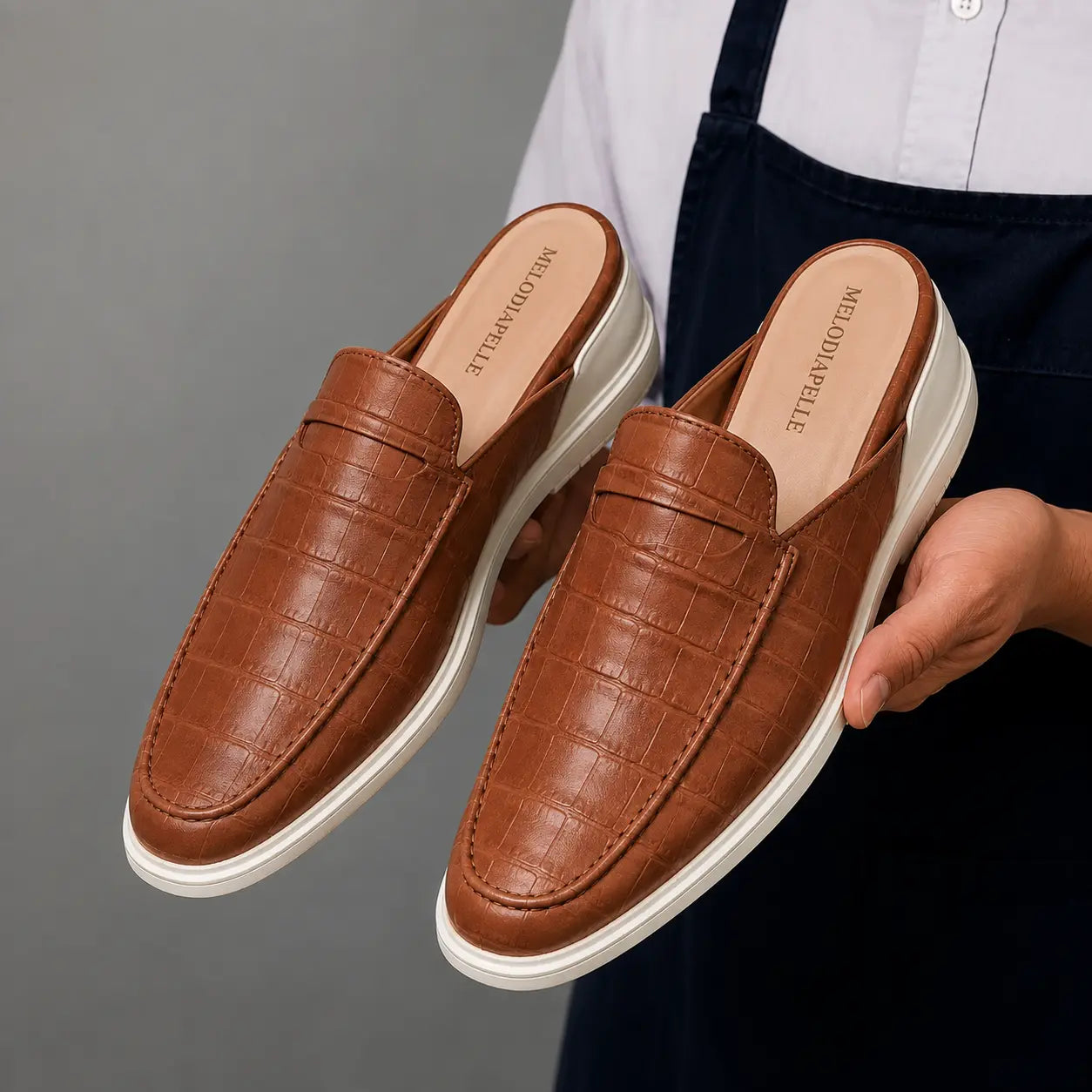 Man holding a pair of Melodiapelle Moreno Mule shoes in tan croc-embossed leather, close-up