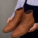 Man holding a pair of Melodiapelle Morocco Cap Toe Combat Boots in tan leather, close-up