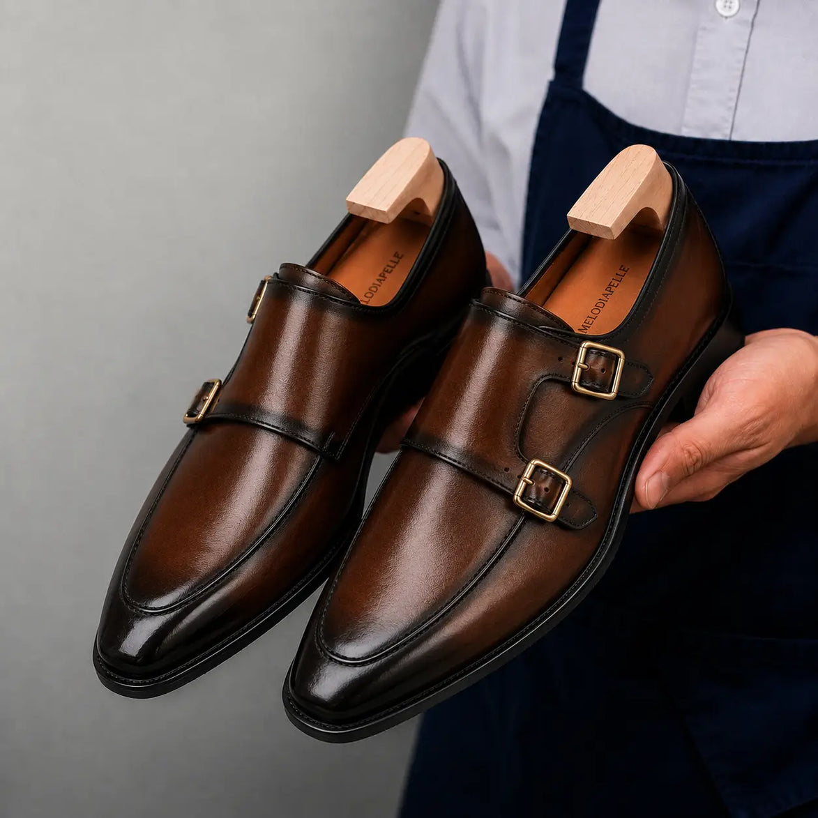 Man holding a pair of Melodiapelle Mortimer Apron Monk Strap shoes in cognac brown leather, close-up