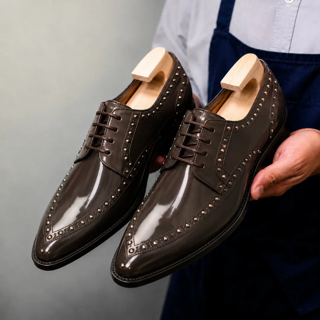 Man holding a pair of Melodiapelle Mortlach Studded Apron Derby shoes in brown leather, close-up