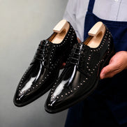Man holding a pair of Melodiapelle Mortlach Studded Apron Derby shoes in nero black leather, close-up