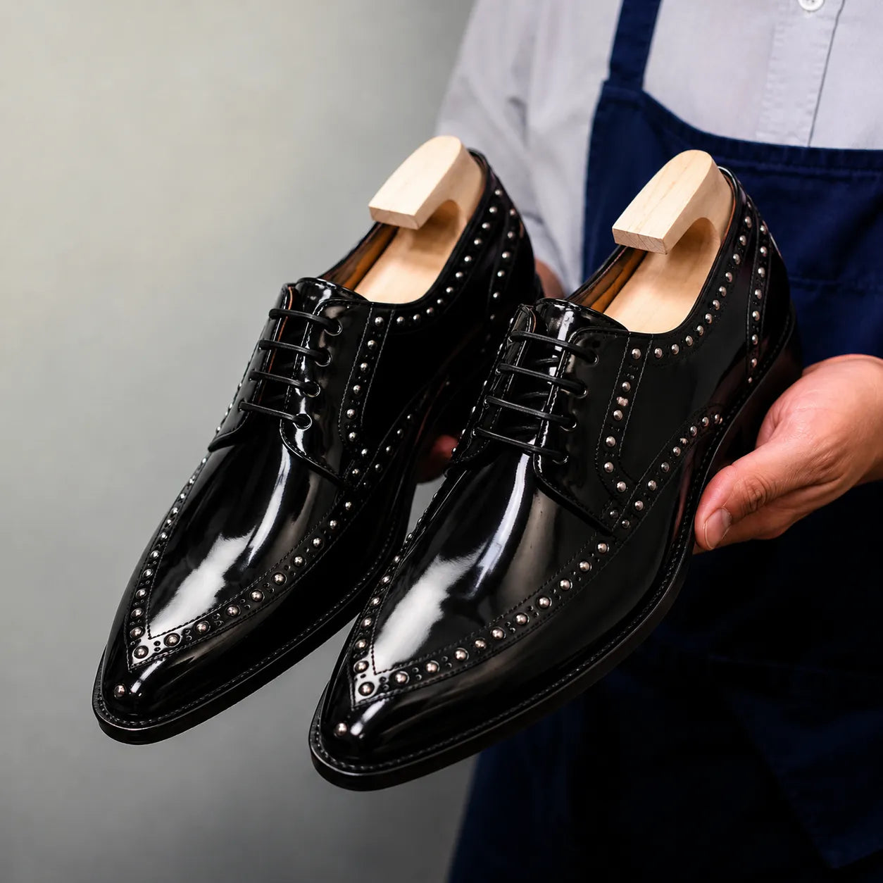 Man holding a pair of Melodiapelle Mortlach Studded Apron Derby shoes in nero black leather, close-up