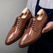 Man holding a pair of Melodiapelle Mortlach Studded Apron Derby shoes in tan leather, close-up