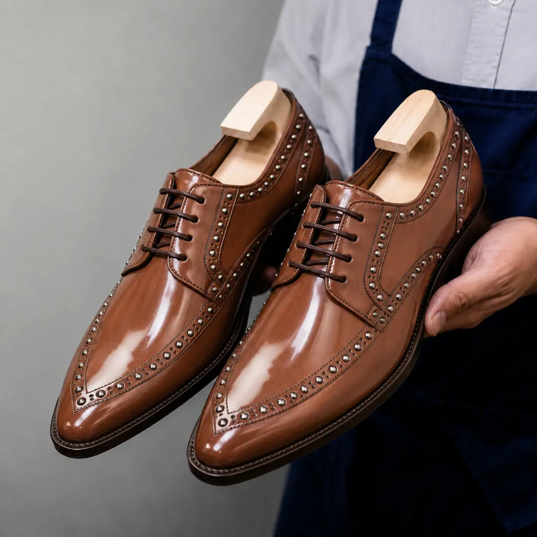 Man holding a pair of Melodiapelle Mortlach Studded Apron Derby shoes in tan leather, close-up