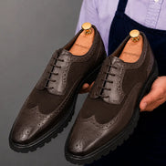 Man holding a pair of Melodiapelle Mosaic Two-Tone Wingtip Derby shoes in brown leather, close-up