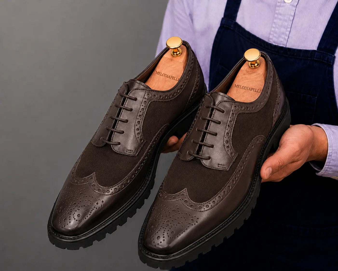 Man holding a pair of Melodiapelle Mosaic Two-Tone Wingtip Derby shoes in brown leather, close-up