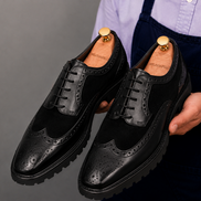 Man holding a pair of Melodiapelle Mosaic Two-Tone Wingtip Derby shoes in nero black leather, close-up
