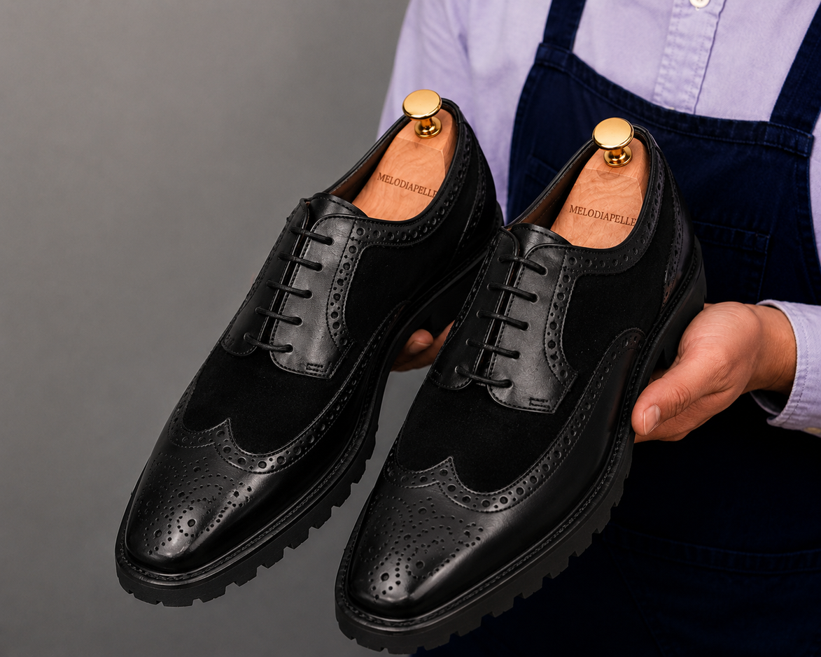 Man holding a pair of Melodiapelle Mosaic Two-Tone Wingtip Derby shoes in nero black leather, close-up