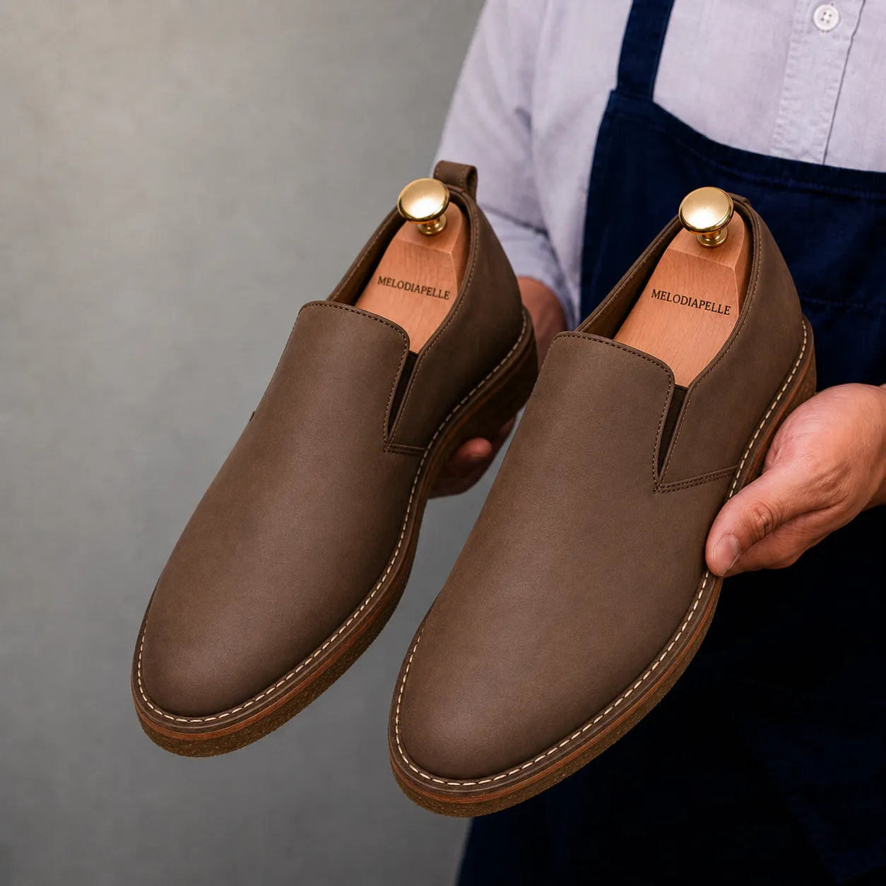 Man holding a pair of Melodiapelle Moscow Opera Slip-On shoes in mole brown nubuck leather, close-up