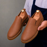 Man holding a pair of Melodiapelle Moscow Opera Slip-On shoes in tan leather, close-up