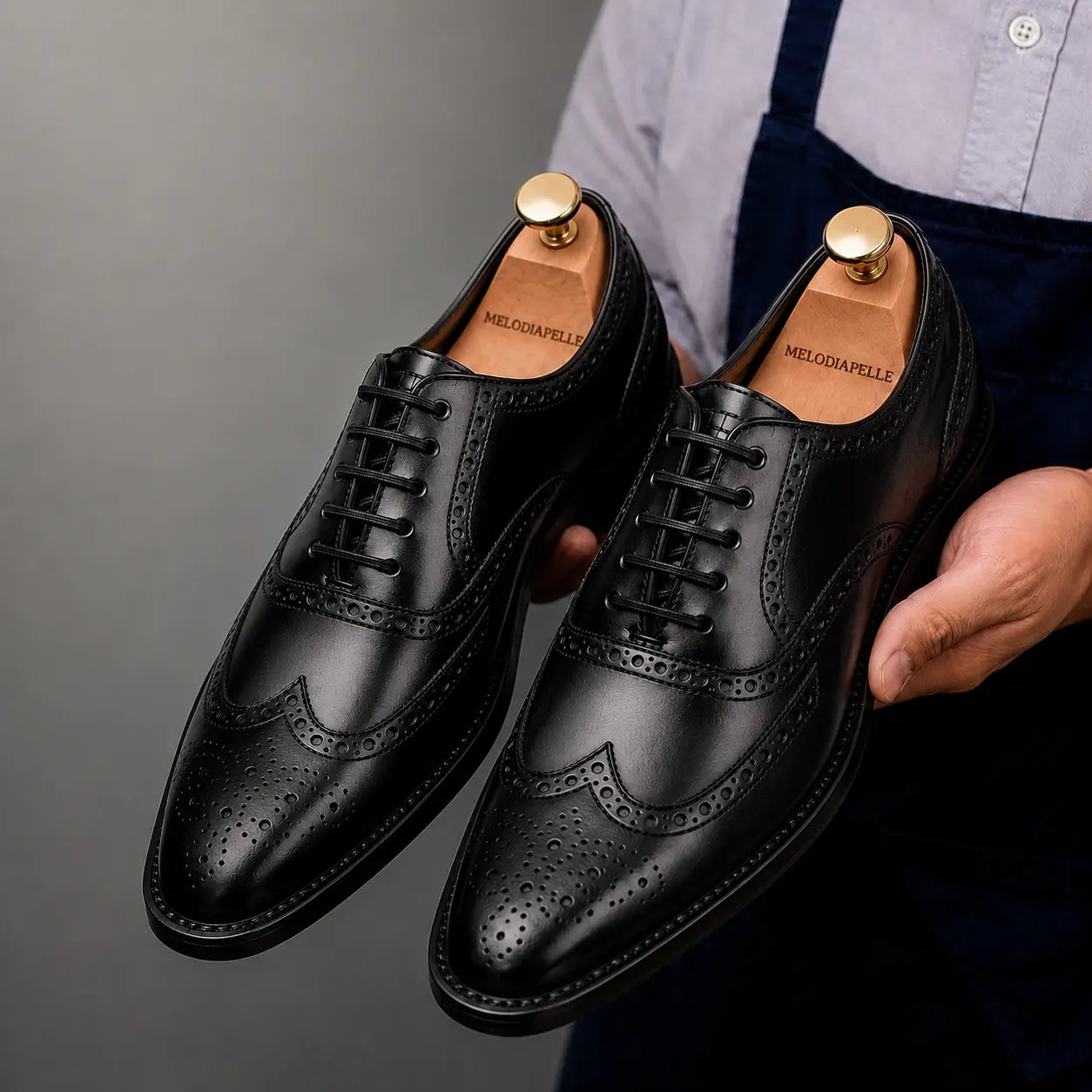 Man holding a pair of Melodiapelle Mossverde Wingtip Brogue Oxford shoes in black leather, close-up