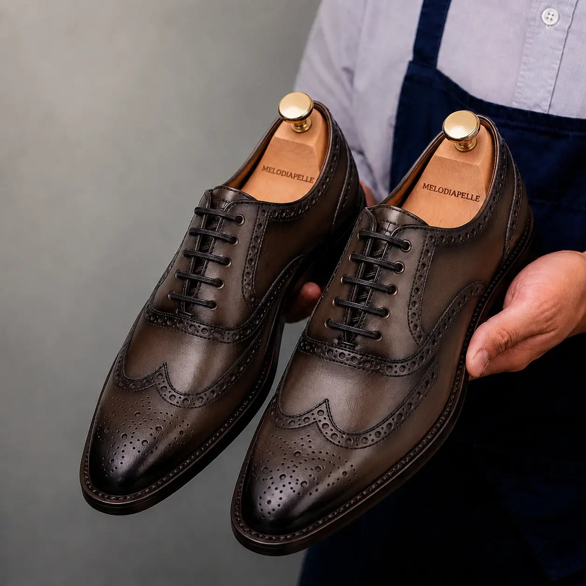 Man holding a pair of Melodiapelle Mossverde Wingtip Brogue Oxford shoes in brown leather, close-up