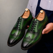 Man holding a pair of Melodiapelle Mossverde Wingtip Brogue Oxford shoes in sage green leather, close-up