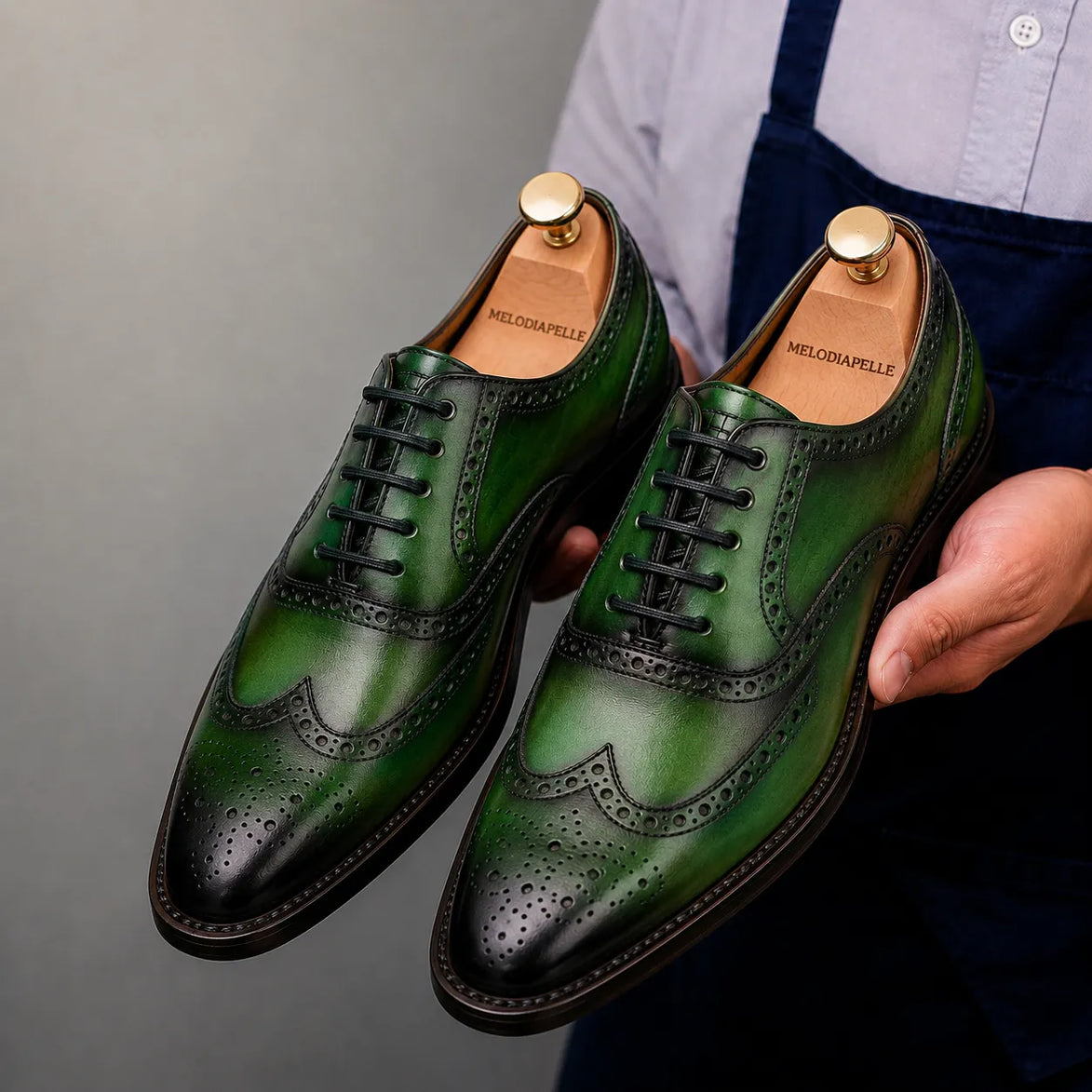 Man holding a pair of Melodiapelle Mossverde Wingtip Brogue Oxford shoes in sage green leather, close-up