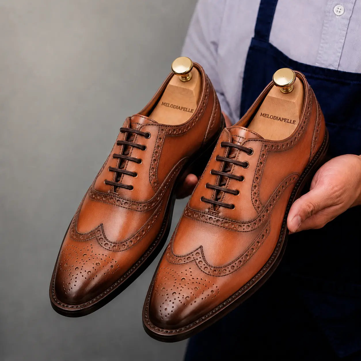 Man holding a pair of Melodiapelle Mossverde Wingtip Brogue Oxford shoes in tan leather, close-up