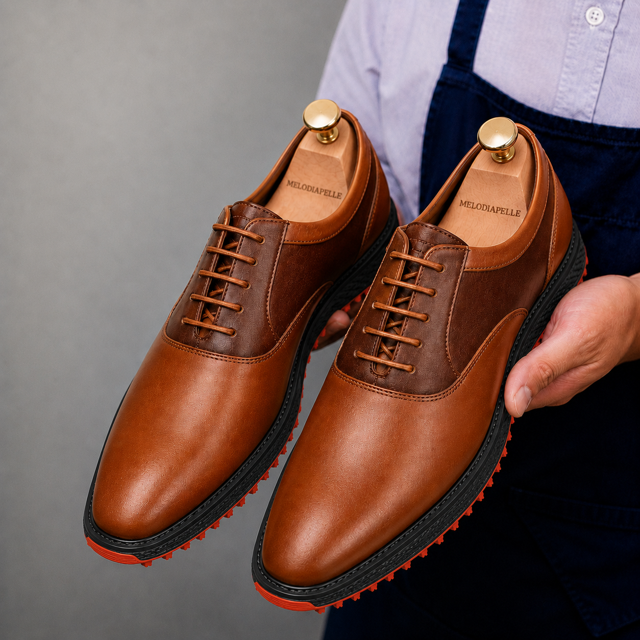 Man holding a pair of Melodiapelle Motif Golf Shoes in tan and dark brown leather, close-up