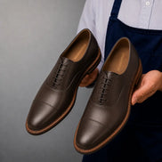 Man holding a pair of Melodiapelle Mount Pleasant Oxford shoes in dark brown leather, close-up